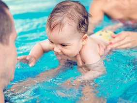 Baby im Schwimmbecken, das von einem Elternteil festgehalten wird