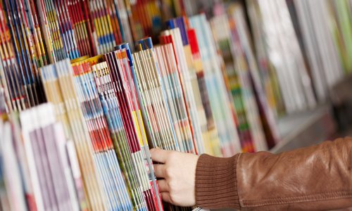 Hand, die nach einer Zeitschrift greift, die mit vielen Zeitschriften in einer Auslage liegt