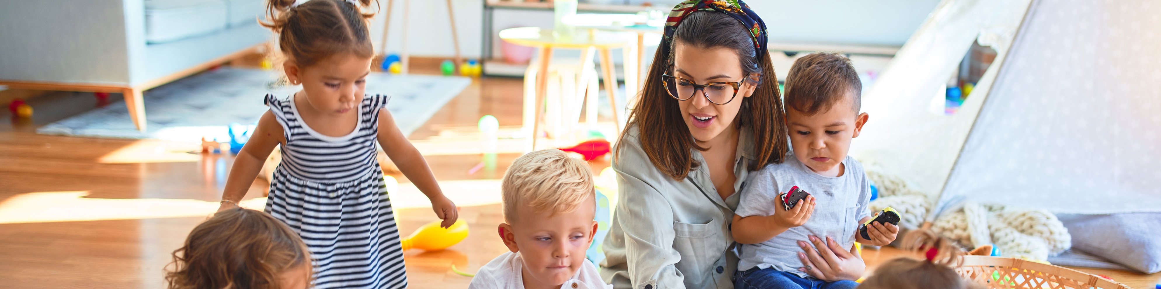 Lehrerin und eine Gruppe Kleinkinder sitzen auf dem Boden und zeichnen mit Papier und Buntstiften