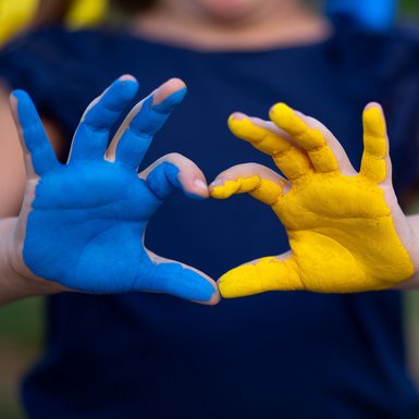 Blau und gelb bemalte Handflächen formen ein Herz