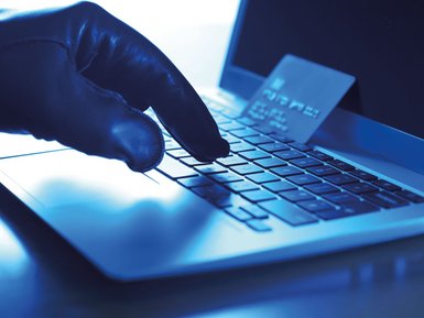 Hand mit schwarzem Lederhandschuh, der an einem Laptop Daten einer Kreditkarte eintippt (Kreditkarte liegt daneben)