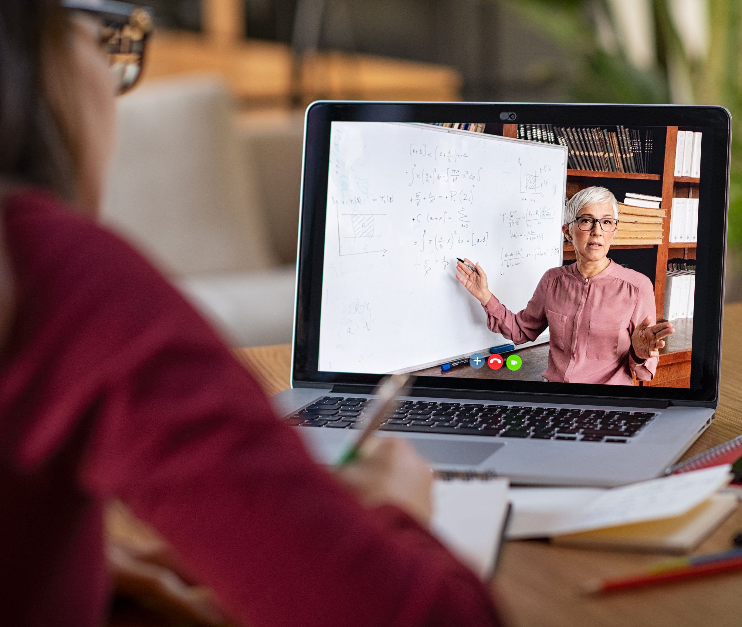 Person sitzt vor Laptop, an dem eine unterrichtende Dozentin zu sehen ist