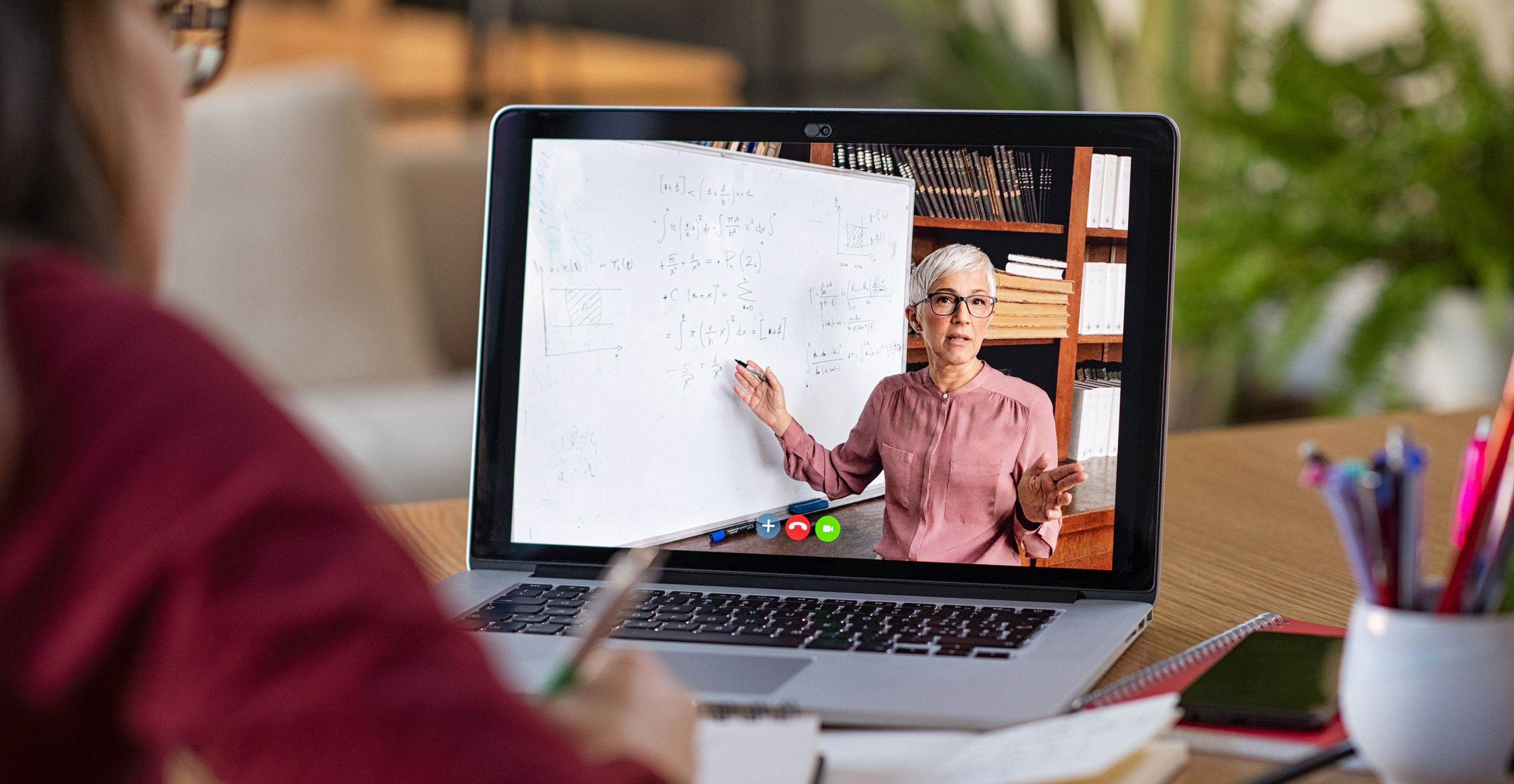 Person sitzt vor Laptop, an dem eine unterrichtende Dozentin zu sehen ist