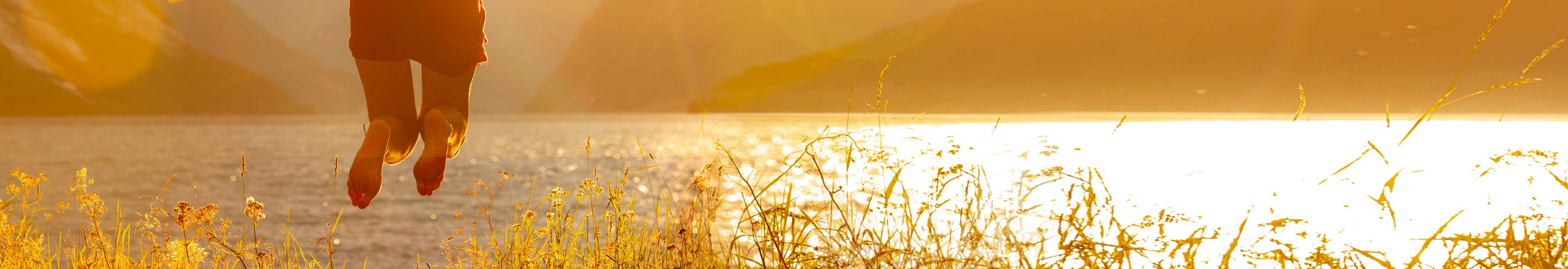 Glückliche springende Frau vor Naturhintergrund am See