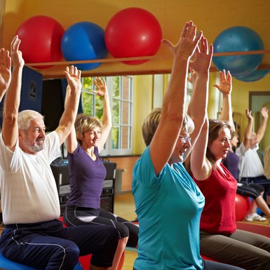 Senioren, die Rückenübungen in einem Fitnessraum machen, auf Sitzball sitzend