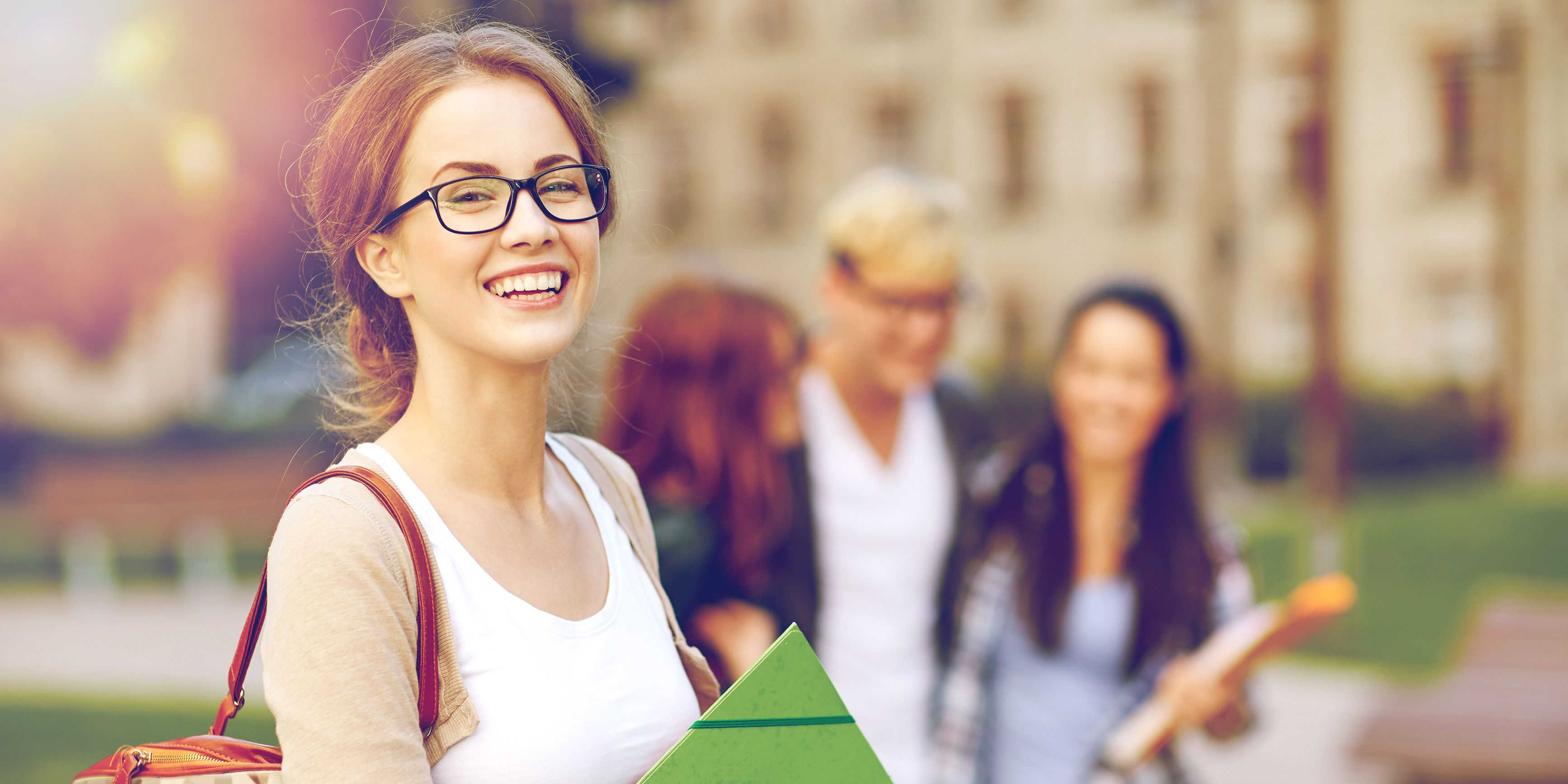 4 Personen, die mit Schultasche oder Schreibtmaterial vor einem Schulgebäude entlang gehen