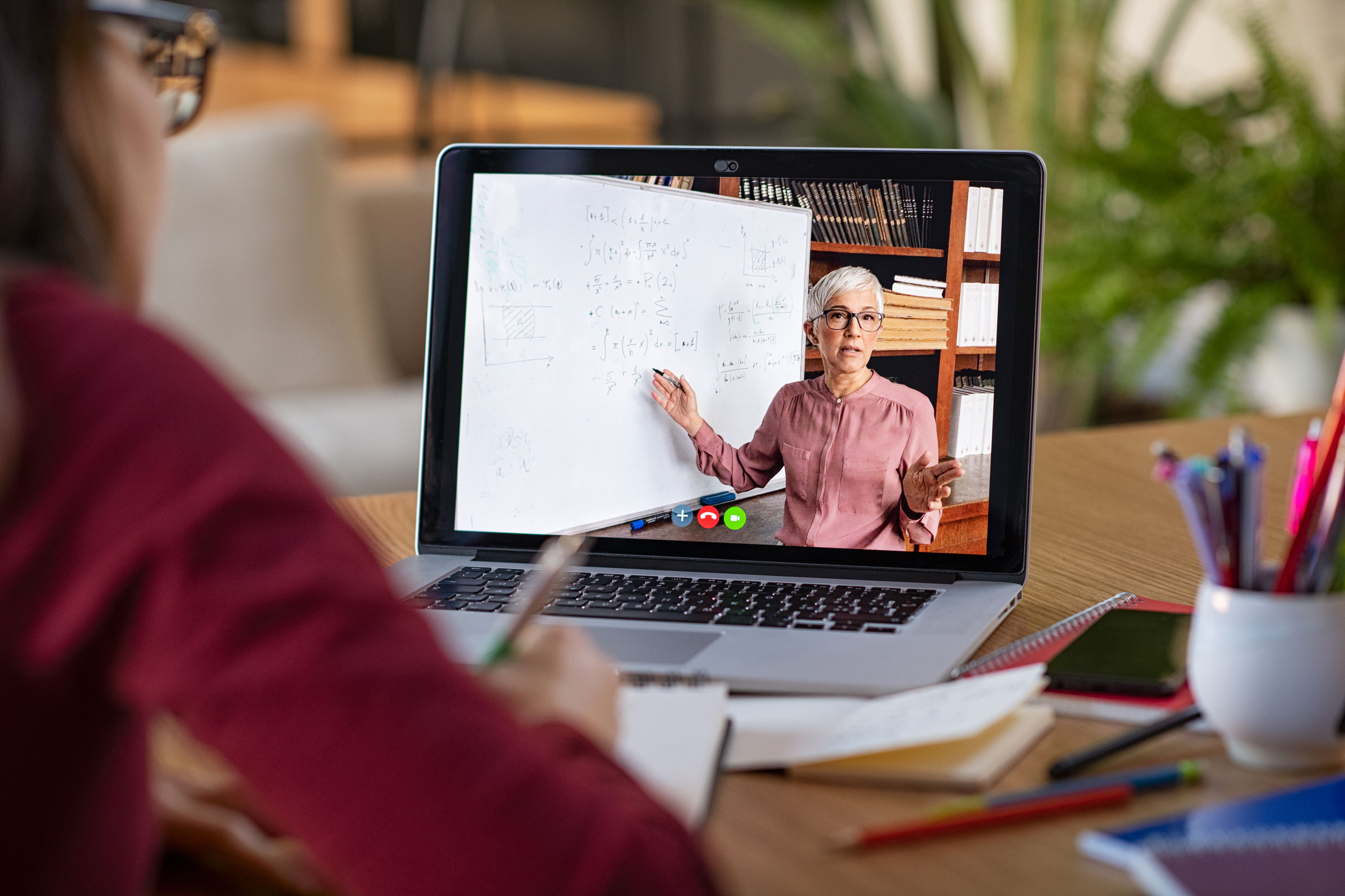 Person sitzt vor Laptop, an dem eine unterrichtende Dozentin zu sehen ist