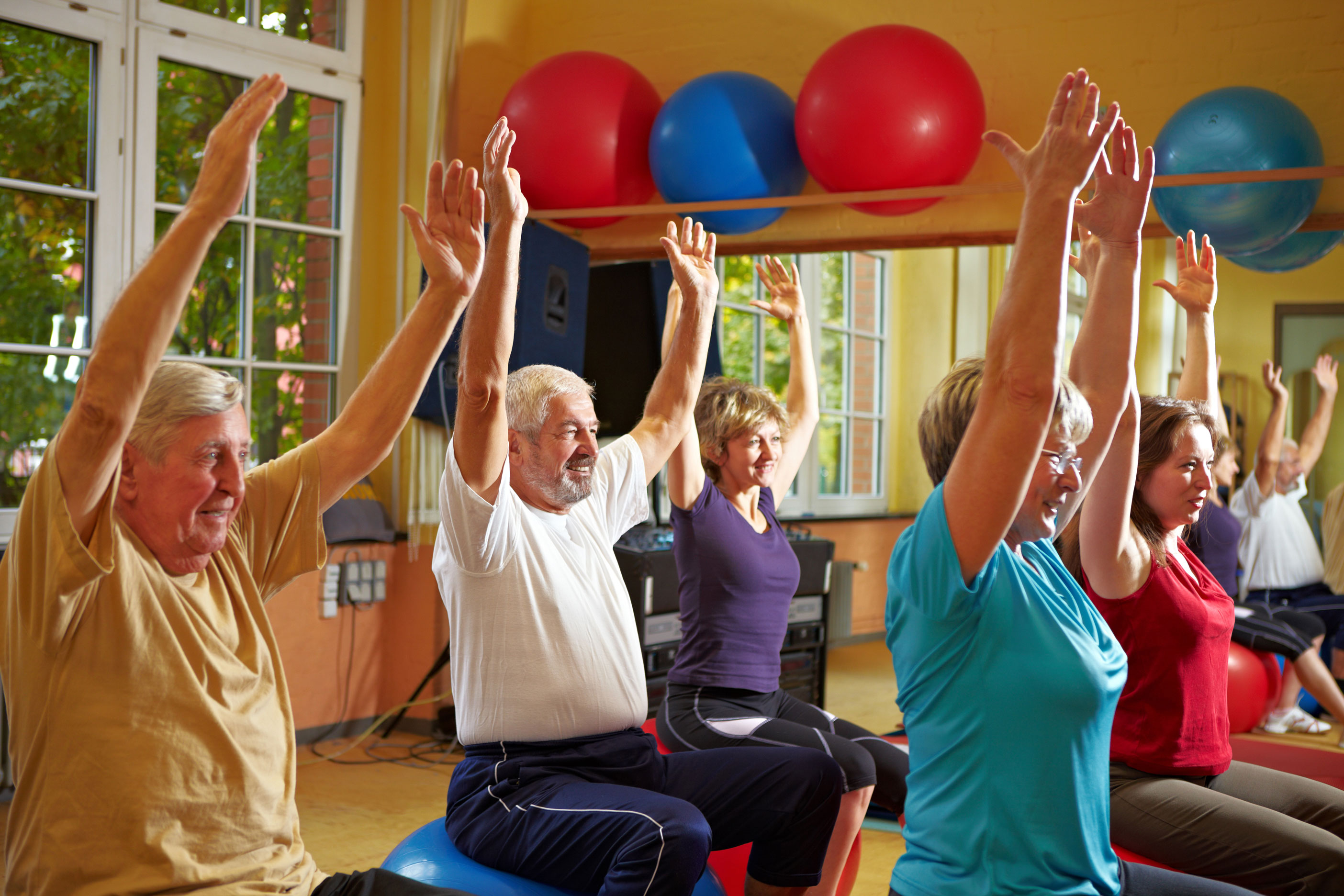 Senioren, die Rückenübungen in einem Fitnessraum machen, auf Sitzball sitzend